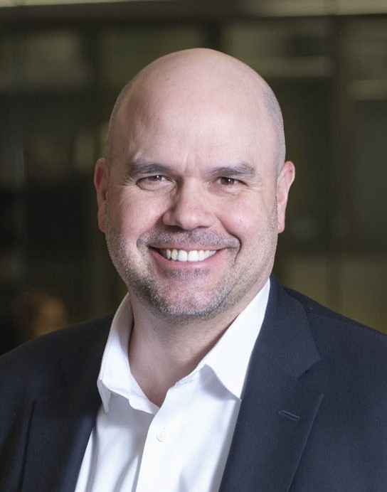 A smiling headshot of a man in a button up and blazer. 