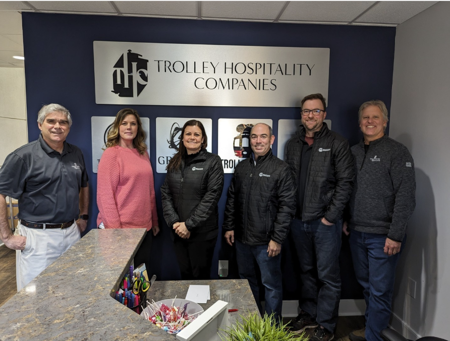 NAMA staff and staff of Trolley Hospitality Companies pose for a photo together in front of the Trolley Hospitality Company sign in their office.