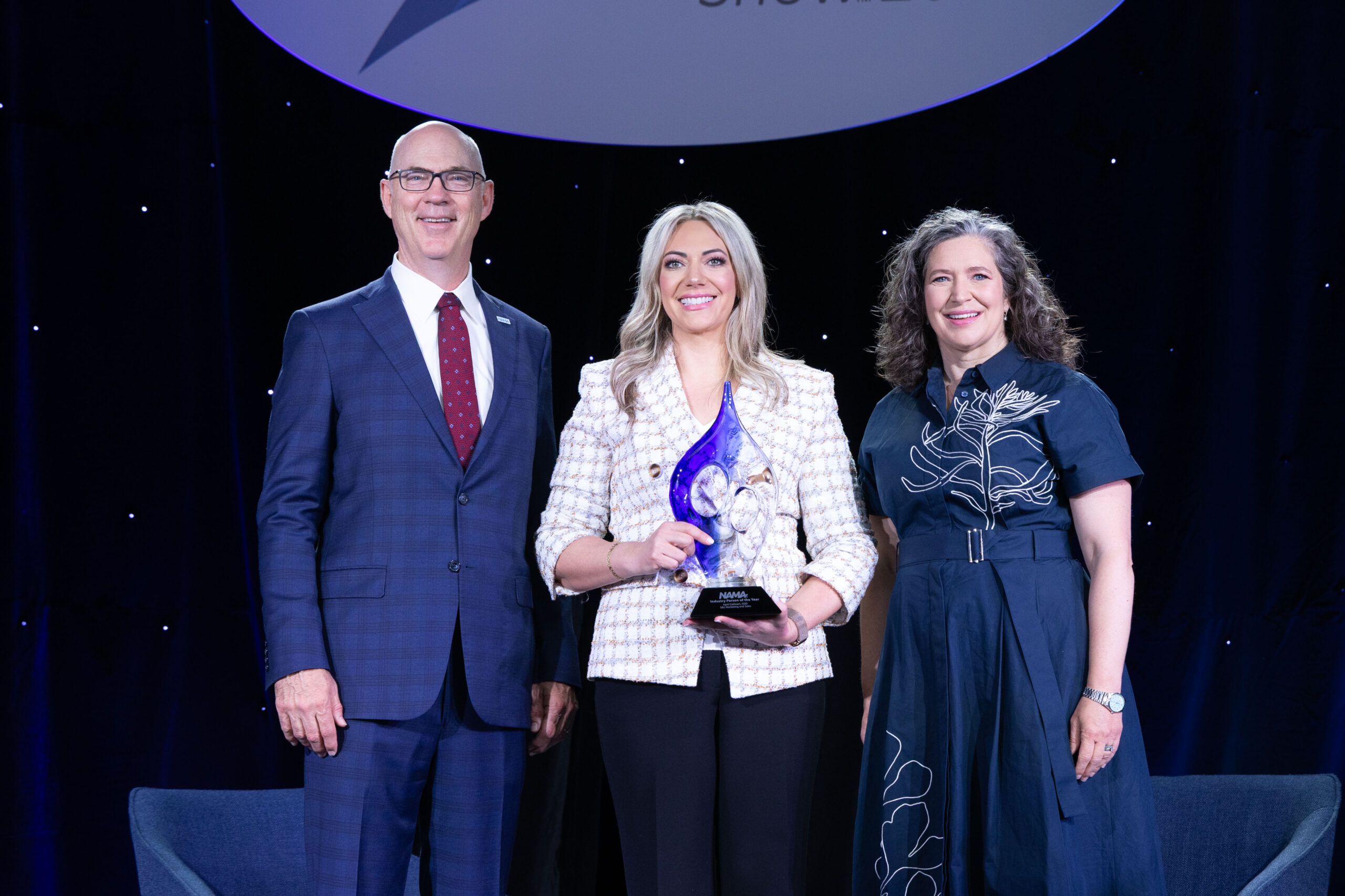 Industry Person of the Year recipient standing in the middle of NAMA Board Chair and NAMA CEO accepting an award.