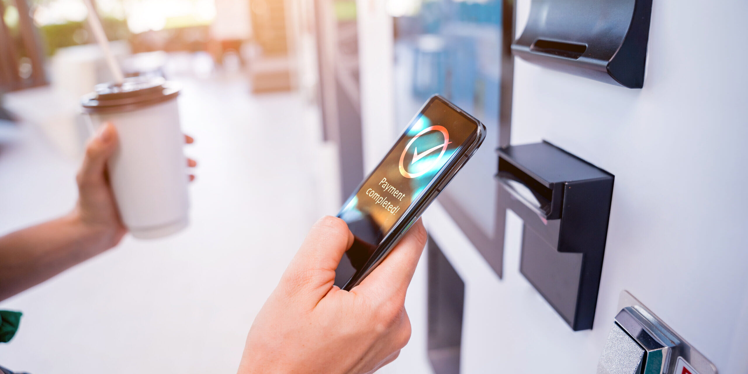 hand holding a phone in front of a kiosk showing successful mobile payment