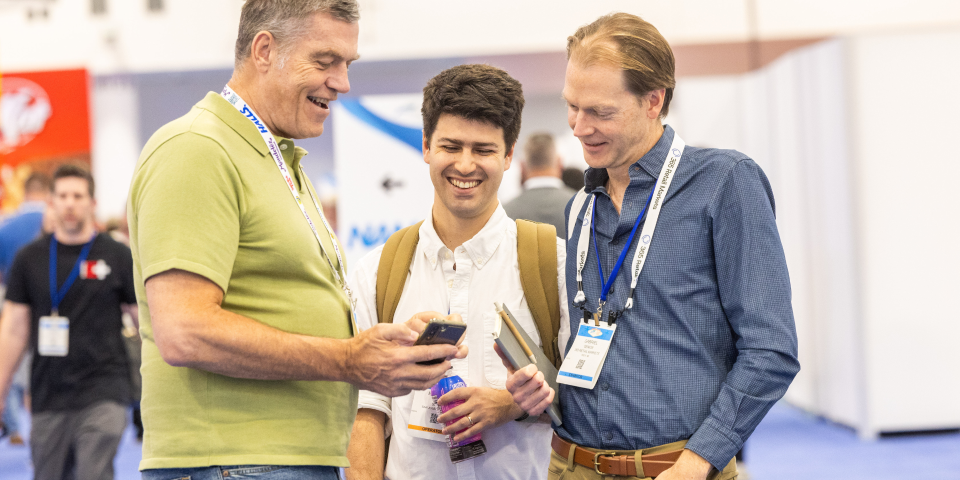 three men smiling looking down at a cellphone