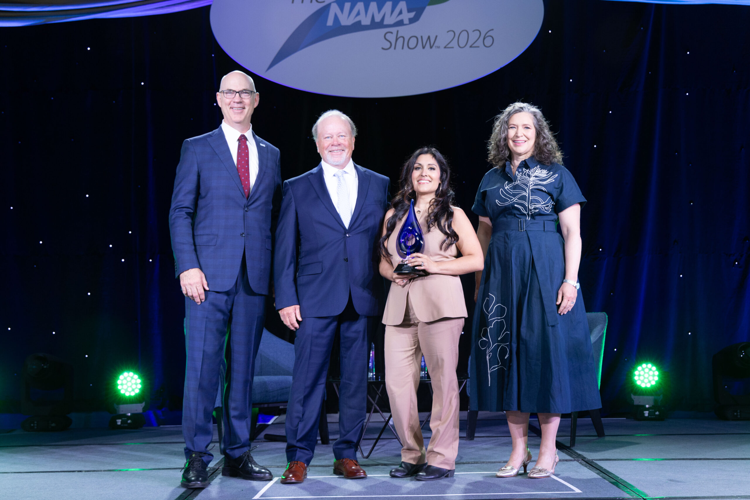 operator of the year representatives stand in the middle of NAMA Board Chair and NAMA CEO accepting the award for Operator of the Year.