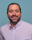 Headshot of a man with light pink button up shirt.